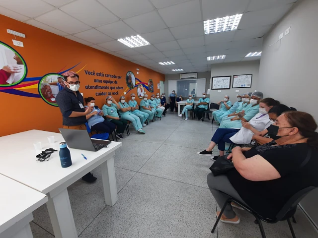 Luiz apresentando para uma equipe de saúde reunida em uma sala de hospital