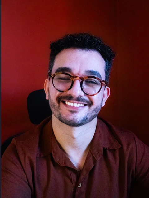 Retrato de Luiz Bezerra sorrindo, de óculos e camisa bordô