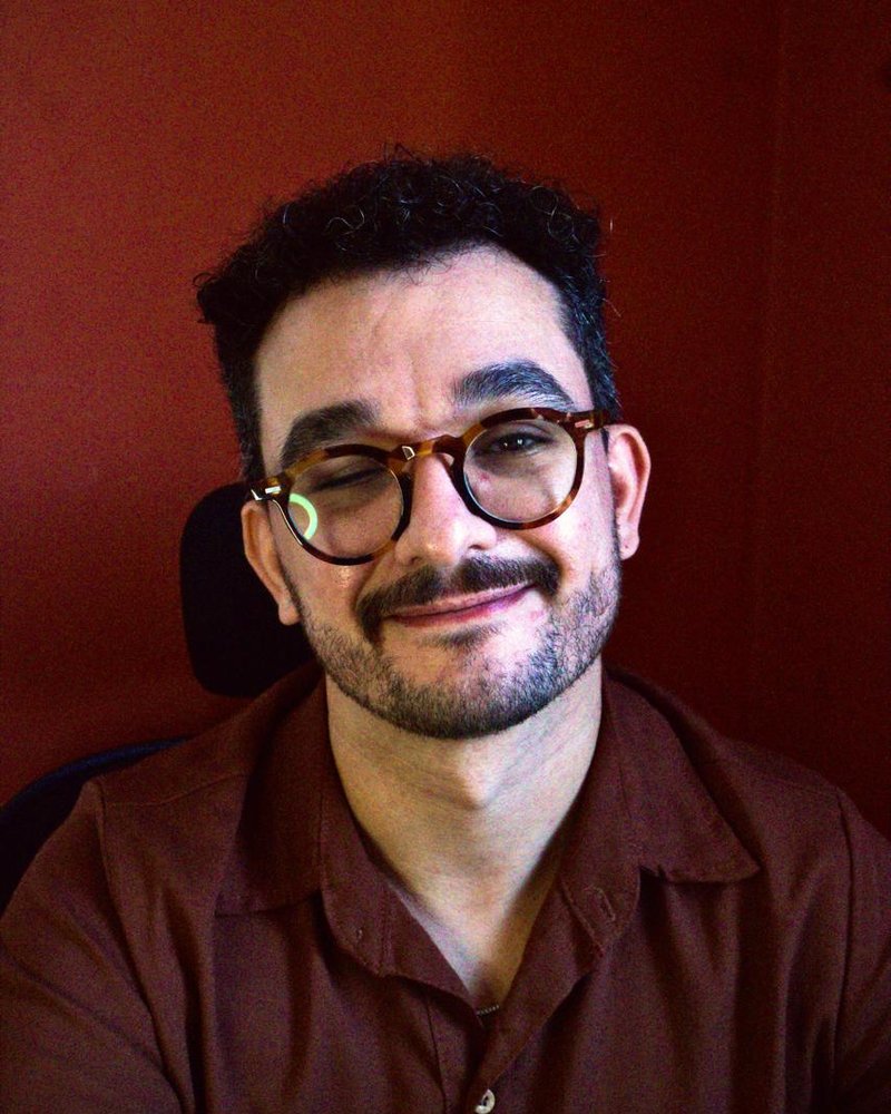Retrato de Luiz Bezerra sorrindo, de óculos e camisa bordô